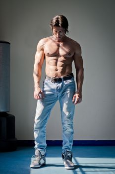 Full figure shot of muscular man shirtless in jeans, looking down