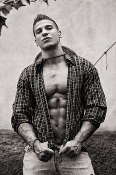 Handsome, muscular young man with open shirt, jeans and straw hat outdoors, black and white shot