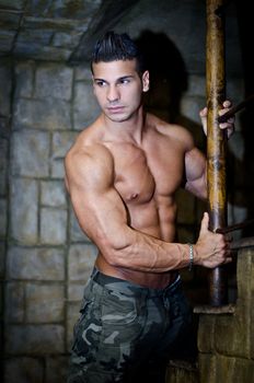 Handsome muscular man shirtless wearing military pants, in front of stone wall