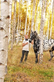 Happy woman with white and black horse in a birch forest