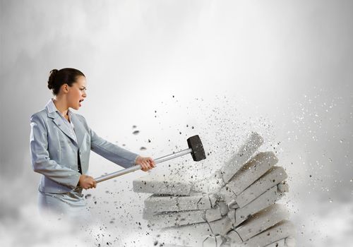 Image of businesswoman breaking bricks with hammer