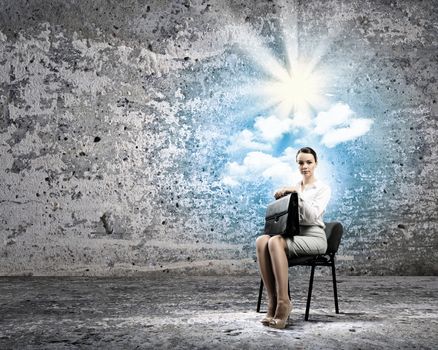 Image of young businesswoman sitting in chair holding suitcase