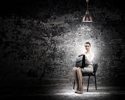 Image of young businesswoman sitting on chair under spot of light