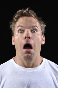 Closeup of scared Caucasian man with eyes and mouth wide open in fear on black background