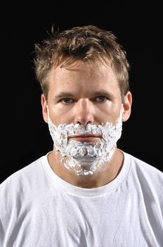 Closeup of handsome Caucasian man with shaving cream on face on black background
