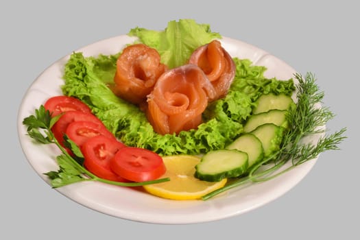 Rolls of red fish fillet with vegetables on the white plate. Isolated on the gray background.