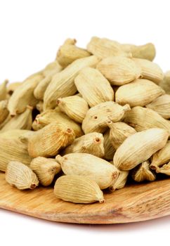 Heap of Cardamom Seeds on Wooden Cutting Board closeup on white background