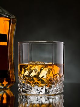 Glass of whisky on the rocks with a bottle