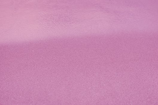 Pink Sandy beach background. Detailed sand texture and water . Top view