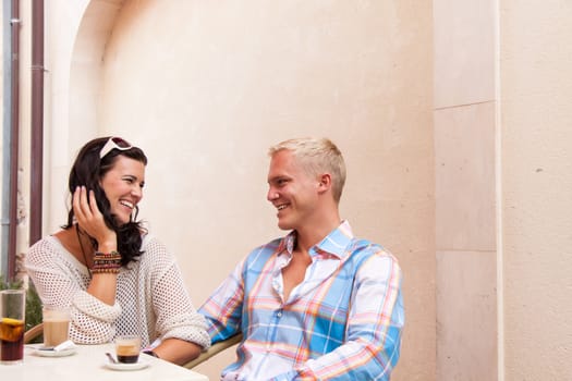 happy young couple sitting outside cafe restaurant drinking coffee  talking summer