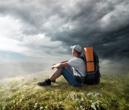 Tourist resting on the hill under storm clouds