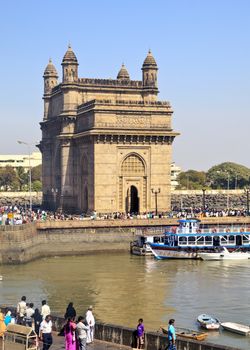 Vertical color portrait of the Gateway to India and the marina with mingling public and day trippers taken from the Ocean View restaurant at the Taj Hotel in Bombay India