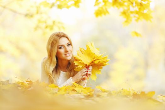 Young woman laying down on the ground covered dry autumnal foliage in beautiful park