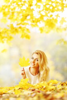 Young woman laying down on the ground covered dry autumnal foliage in beautiful park