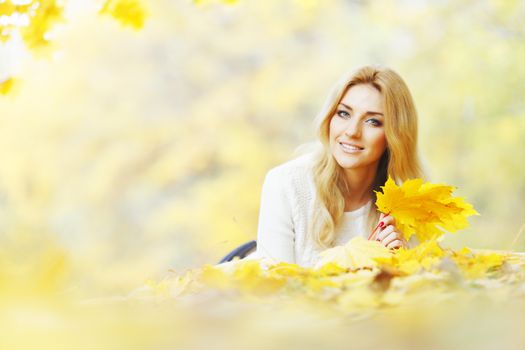 Young woman laying down on the ground covered dry autumnal foliage in beautiful park