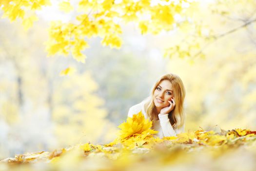 Young woman laying down on the ground covered dry autumnal foliage in beautiful park