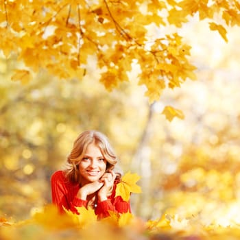 Happy young woman laying on autumn leaves in park