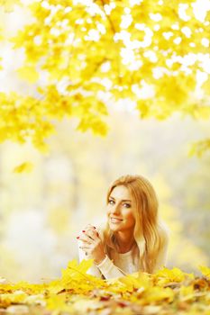 Young woman laying down on the ground covered dry autumnal foliage in beautiful park