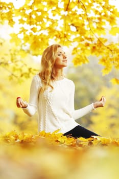 Beautiful young woman meditating outdoors in autumn park