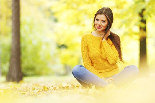 Beautiful woman sitting on autumn leaves in park