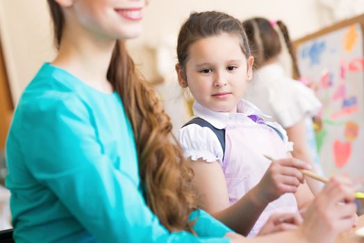 girl interested in drawing the teacher in the background paint other children