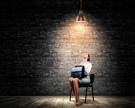 Image of young businesswoman sitting on chair under spot of light