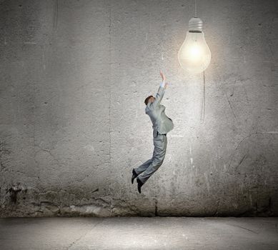Image of young businessman jumping and catching light bulb