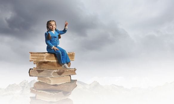 Image of cute school girl in sitting on pile of books