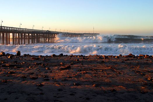 Ocean waves throughout at storm crashing into a wooden pier.