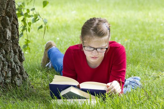 Young girl reading book in park in spring day