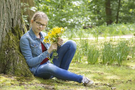 Smiling girl with big bouquet of spring flowers sitting in the park