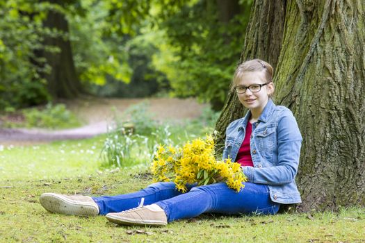 Smiling girl with big bouquet of spring flowers sitting in the park