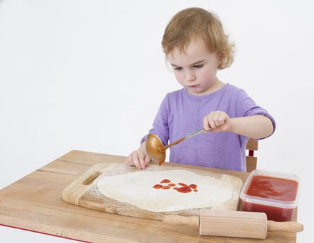 little girl making pizza. studio shot on light grey background