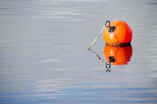 Orange buoy on a rope swimming on water