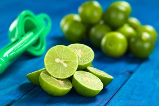 Lime halves on blue wood with squeezer in the back (Selective Focus, Focus on the lime half on the top) 