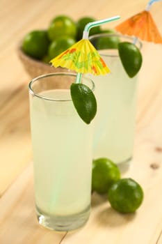 Freshly prepared refreshing lemonade out of limes in tall glass garnished with lime wedge and paper parasol (Selective Focus, Focus on the lime wedge)