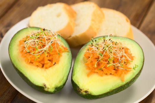 Avocado halves filled with grated carrot and sprinkled with alfalfa sprouts served on plate with baguette slices (Selective Focus, Focus on the front of the grated carrot) 