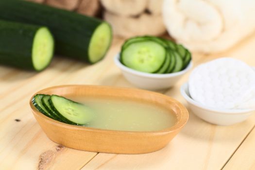 Homemade natural cucumber facial toner that hydrates, softens, soothes and cleanses the skin in a wooden bowl with cucumber slices, with facial pads and towels (Selective Focus, Focus on the front of the cucumber slices in the toner)