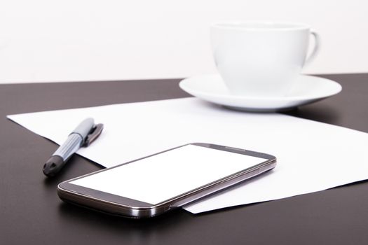 Smart phone with blank, white screen, ceramic coffee cup, pen and empty paper on wooden table, isolated on white background.