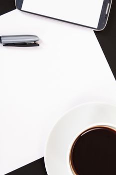 Smart phone with blank, white screen, ceramic coffee cup, pen and empty paper, top view on wooden table.