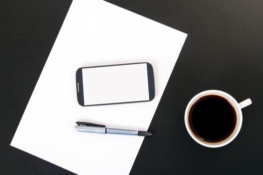 Smart phone with blank, white screen, ceramic coffee cup, pen and empty paper, top view on wooden table.