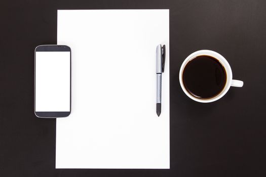 Smart phone with white, blank screen, empty paper, pen and black coffee in white cup on wooden table.