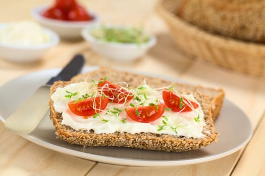 Wholewheat bread spread with cream cheese, with cherry tomato and alfalfa sprouts on top served on plate (Selective Focus, Focus on the tomato in the front) 