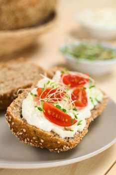 Wholewheat bread spread with cream cheese, with cherry tomato and alfalfa sprouts on top served on plate (Selective Focus, Focus on the tomato in the front) 