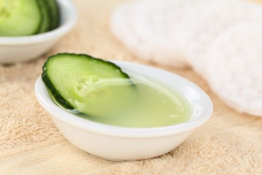 Homemade natural cucumber facial toner that hydrates, softens, soothes and cleanses the skin in a bowl with a cucumber slice, with facial pads on towel (Selective Focus, Focus on the front of the cucumber slice in the toner)