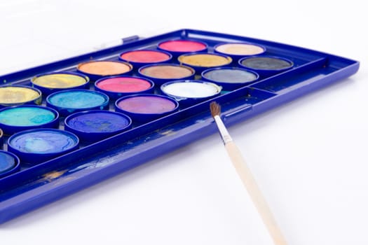 Close up of messy water color paint box and thin brush, isolated on white.