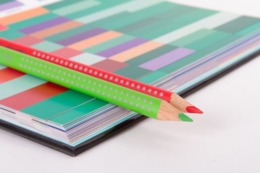 Red and green pencils on colorful art palette book, isolated on white background.
