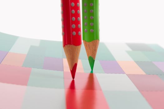Red and green pencils standing on colorful art book, isolated on white background.
