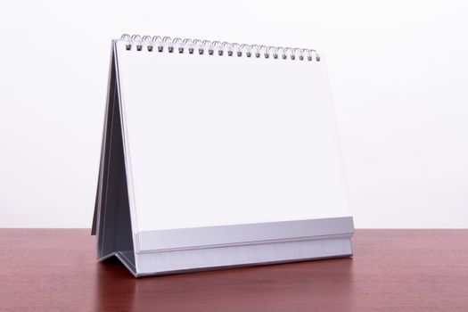 Single blank desk calendar on wooden table, isolated on white background.