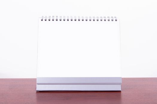 Single blank desk calendar on wooden table, isolated on white background.